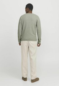 Pull en maille vert clair avec un col rond, associé à un pantalon beige clair ample. Des chaussures aux tons terre complètent l'ensemble.