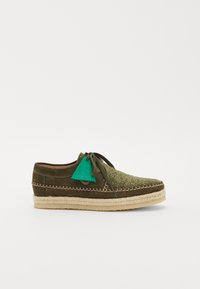 Espadrille en suède vert avec une tige en tissu texturé, lacets assortis et couture décorative. Présente une semelle en jute.