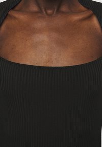 Černý žebrovaný top s vykrojeným výstřihem a strukturovanou tkaninou. Design zdůrazňuje přiléhavý tvar a hladké přechody v látce.