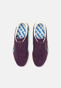 Tenisky Reebok s fialovým semišovým svrškem, zelenými akcenty, hnědou gumovou podrážkou a bílým vnitřkem s modrým tiskem loga.
