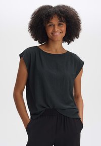 Blusa nera a maniche corte con scollatura rotonda e tessuto testurizzato. Caratterizzata da una vestibilità rilassata e un dettaglio arricciato in vita.
