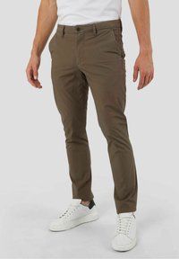Chinos marron en coton, avec une coupe slim, des poches latérales et une fermeture à bouton, assortis à des baskets blanches.