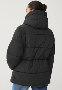 Giacca a vento nera con un colletto alto, design trapuntato e vestibilità leggermente ampia. Texture morbida con una superficie liscia.
