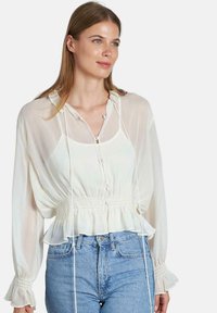 Witte, lichte blouse met capuchon, knoopsluiting aan de voorkant en elastische taille. Beschikt over lange, geplooide mouwen en een soepele, iets doorschijnende textuur.