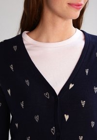 Cardigan navy con cuori crema e motivi di coni gelato, design a V, chiusura con bottoni, indossato sopra una maglietta rosa chiaro.