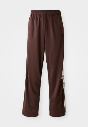 Bordeauxkleurige Adidas trainingsbroek met elastische tailleband en witte zijstrepen, voorzien van het Adidas-logo en tekst op het linkerbeen.