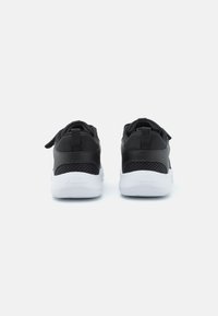 Des chaussures de sport noires avec un dessus lisse, des panneaux latéraux en maille et des semelles en caoutchouc blanches. Elles possèdent des languettes de traction et un logo discret sur le talon.