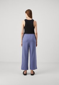 Crna majica bez rukava u kombinaciji s svijetloplavim hlačama širokih nogavica s elastičnom waistband i teksturiranom završnom obradom. Jednostavne crne sandale.
