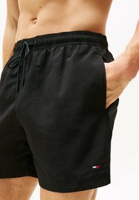 Pantaloni da bagno neri realizzati in tessuto leggero. Presentano una vita elasticizzata, cordoncino e tasche laterali. Include un piccolo dettaglio con logo.