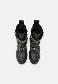 Botas de cuero negro hasta el tobillo con detalles de tachuelas plateadas y hebillas. Tienen una textura suave y un diseño de punta redonda. Tacón reforzado.