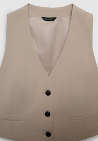 Gilet beige a scollo a V con una texture liscia, caratterizzato da quattro bottoni neri e due tasche laterali. L'interno è foderato con un tessuto chiaro.