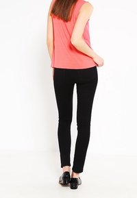 Top sans manches corail à coupe décontractée associé à un jean skinny noir et des chaussures noires. Le top présente un design à ourlet arrondi.