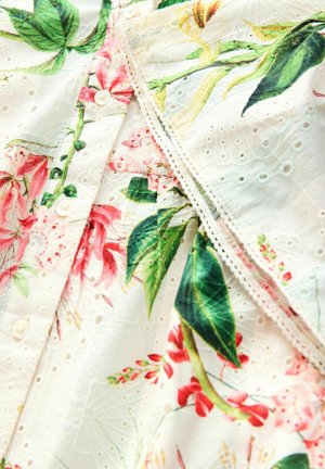 Tessuto a fiori in bianco presenta foglie rosa e verdi, una texture ad occhio intricato e piccoli bottoni rotondi lungo una cucitura.