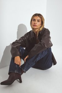 Brahms ādas jaka ar plašu apkakli, savienota ar ziliem džinsiem un bordo krāsas augstpapēžu kurpēm ar izteikto purngalu. Gludas tekstūras un strukturēts dizains.