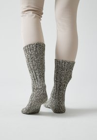 Calze lavorate a maglia grigie e bianche con un design testurizzato a coste, che arrivano a metà polpaccio; abbinate a leggings di un beige chiaro.