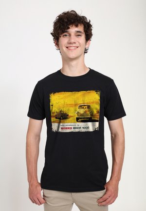 Sort t-shirt med et vintage bilgrafik i gul og hvid, med teksten "Morris Minor 1000", sat imod en tekstureret baggrund.