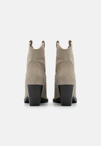 Botines de ante gris con un alto tacón negro grueso y parte superior con corte. Presentan líneas limpias y un diseño minimalista sin herrajes visibles.
