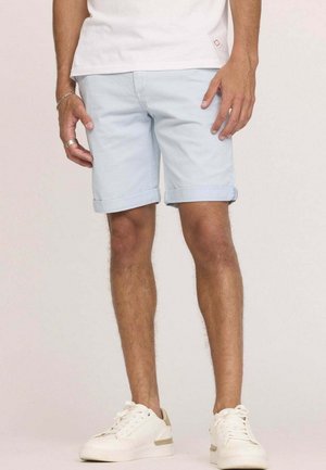 Shorts en denim bleu clair avec des ourlets retroussés, présentant un design classique. Portés avec des baskets blanches, sur un fond uni.