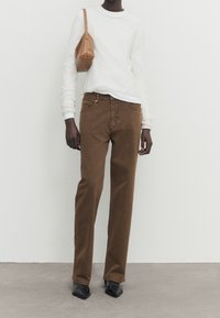 Bruna raka jeans i ben, kombinerat med en vit långärmad skjorta och en beige axelväska, bärs med svarta spetsiga skor.