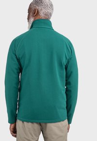 Grüne Fleecejacke mit hohem Kragen, langen Ärmeln und einer glatten Textur, mit einem verlängerten Rückensaum für zusätzlichen Schutz.