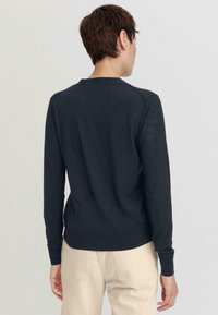 Pull en tricot bleu marine foncé avec de longues manches et un col rond. Doté de poignets et d'un ourlet côtelés, texture lisse avec une silhouette ajustée.