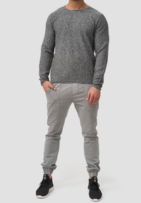 Maglietta grigia a maniche lunghe in maglia con scollo tondo; abbinata a pantaloni jogger grigi chiari con polsini elasticizzati e tasche laterali. Sneakers nere.