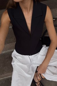 Must värv, ilma varrukateta, keha ülikond, millel on sügav V-kuju kaelus ja teravad kraed, koos lõvide valgete pükstega ja mustade rihmadega kingadega.