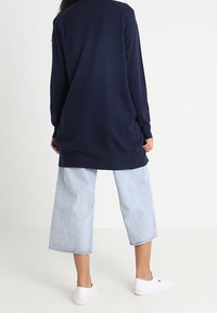 Marinblå långärmad tröja med en avslappnad passform, kombinerad med ljusblå vida cropped jeans. Vita skor fulländar outfiten.