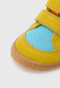 Κίτρινο σουέντ παπούτσι με μπλε λεπτομέρειες από δίχτυ, διαθέτει δύο ιμάντες με βέλκρο και καφέ λάστιχο σόλα, στρογγυλεμένη μύτη και αντίθετη ραφή.