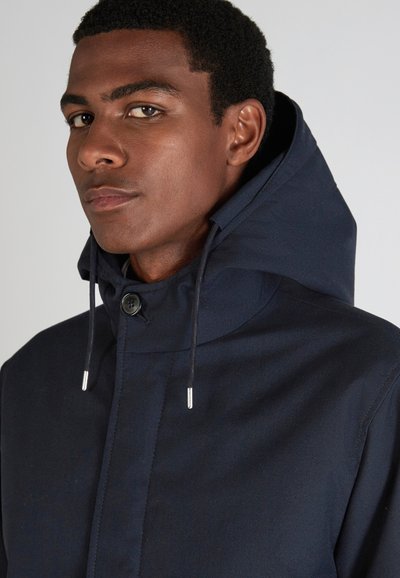 Navy hooded jacket with a high collar, button fastening, and drawstrings. Smooth texture with minimal seams, showcasing a contemporary design.