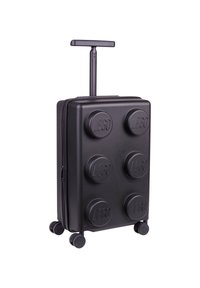 Black suitcase shaped like a LEGO brick, featuring six raised circular studs, a telescopic handle, and four wheels for easy mobility.