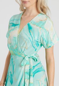 Un vestido envolvente de color verde claro con escote en V, manga corta y un patrón de mármol dorado. Presenta una cintura anudada y una textura suave y fluida.