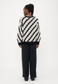 Maglione lavorato a maglia in crema e nero con righe diagonali, caratterizzato da una vestibilità ampia, polsini e orlo a costine. Indossato con pantaloni neri a gamba larga.