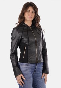 Giacca di pelle nera con un design aderente, cappuccio e dettagli in zip dorata; presenta pannelli in tessuto a contrasto e tasche laterali con zip.