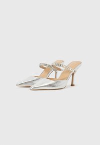 Silver metallic pointed-toe slingback heels with a slim heel and ruffled strap detail. Smooth texture, minimalist design.
