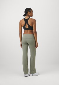 Sujetador deportivo negro con diseño de espalda nadadora y detalle recortado, combinado con pantalones ajustados de campana en color verde oliva. Zapatillas blancas con detalles coloridos.
