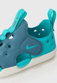 Nike barnsandaler i mörkblått och teal. Tillverkade av gummi, har ventilationshål, en strukturerad sula och en tygrem för säker passform.