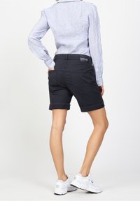 Tmavě modré džínové šortky s ohrnutými lemy, opatřené zadními kapsami a páskem s logem značky. Kombinovány s pruhovaným tričkem s dlouhým rukávem.