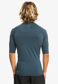 Short-sleeve athletic top in a dark teal color, featuring a smooth texture and a fitted design with raglan sleeves and a small logo detail.