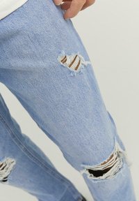 Jeans de denim azul claro desgastados, con grandes desgarros desgastados en las rodillas y una tela texturizada con un ligero desvanecimiento.