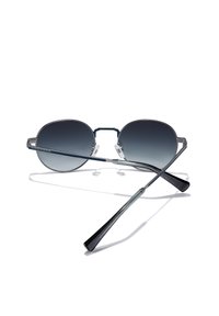 Ümarad päikeseprillid läbipaistva raamiga, tumenevate läätsedega, hõbedaste detailidega ja õhukeste metallist sangadega. Varustatud reguleeritavate ninasangaribade ja mustade otsikutega.