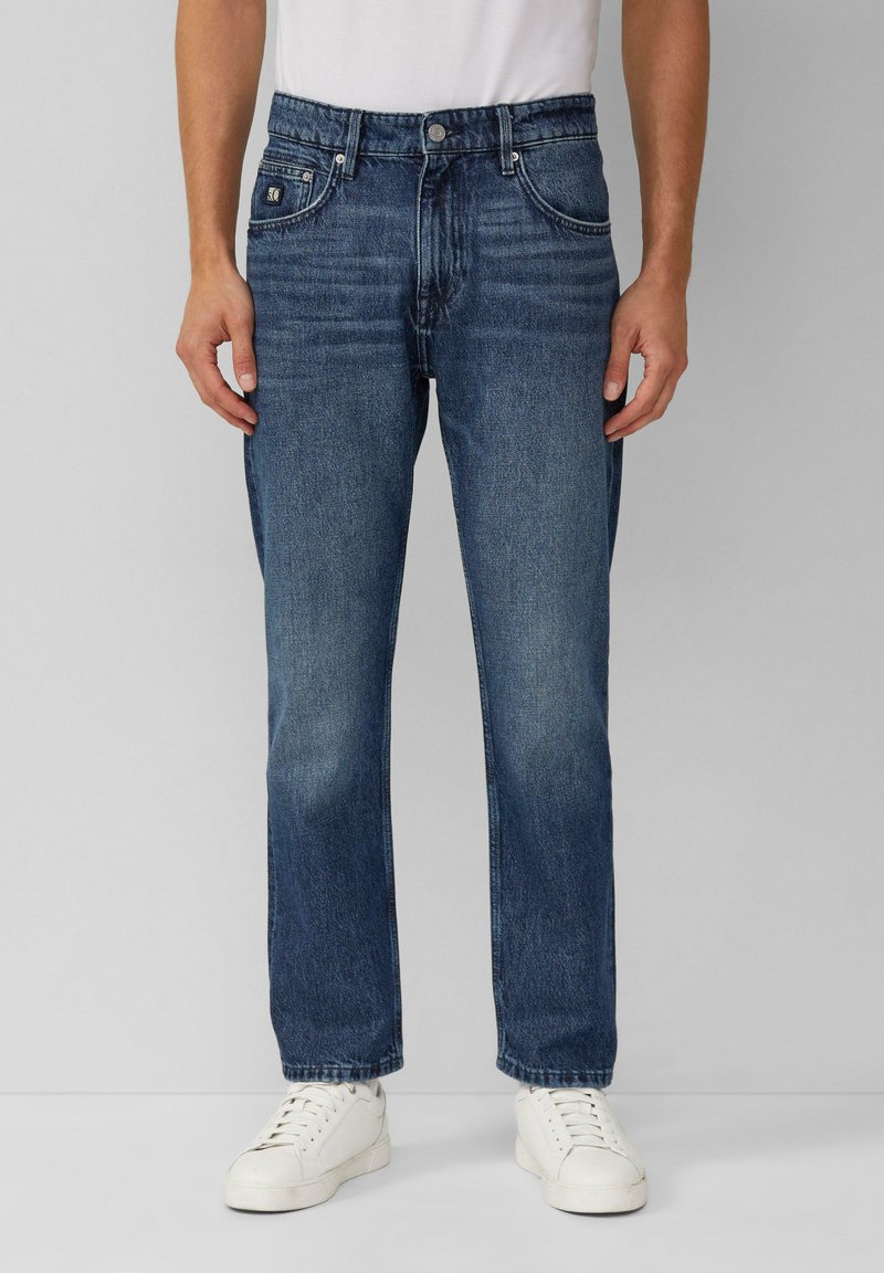 Jeans in denim blu scuro con vestibilità dritta, design a cinque tasche e leggera scoloritura. Abbinati a una t-shirt bianca e sneakers bianche.