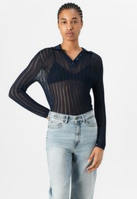 Polo a maniche lunghe di colore navy con un design a maglia testurizzata e stampata, presenta bottoni sul colletto ed è abbinato a jeans in denim azzurro chiaro.