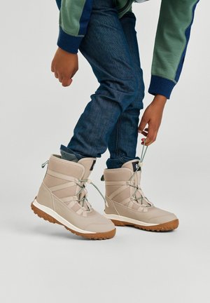 Beige wasserdichte Stiefel mit strukturiertem Stoff und verstärkter Zehenpartie. Verfügt über grüne Schnürsenkel, gepolsterten Schaft und eine rutschfeste Gummisohle.