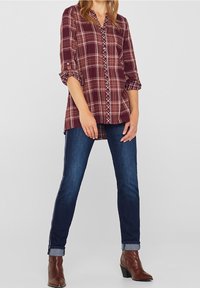 Rød- og brunternet skjorte med knaplukning, opkrøllede ærmer, parret med mørkeblå jeans. Brune ankelstøvler fuldender outfittet.