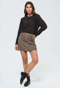 Pull en laine noir avec un motif texturé associé à une mini-jupe écossaise marron à fermeture à boutons sur le devant. Chaussures et chaussettes noires.