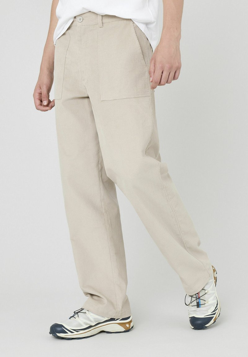 Pantalons beige texturés à coupe décontractée, dotés de deux poches avant et d'une fermeture à bouton unique, associés à des chaussures légères.