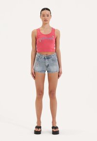 Top corto rojo sin mangas con diseño bordado en azul, combinado con pantalones cortos de mezclilla de tiro alto en un azul claro que cuentan con costuras decorativas. Sandalias de plataforma negras.