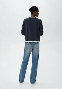 Dark gray sweatshirt with cut-out shoulder design, paired with light blue straight-leg jeans featuring back pockets. Smooth texture.