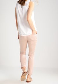 Witte mouwloze top met een sleutelgat aan de achterkant; lichtroze nauwsluitende broek met omslagen aan de enkel; beige flats met een kleine hak. Eenvoudig en op maat gemaakt ontwerp.